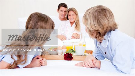 Caucasian family having breakfast sitting on bed at home