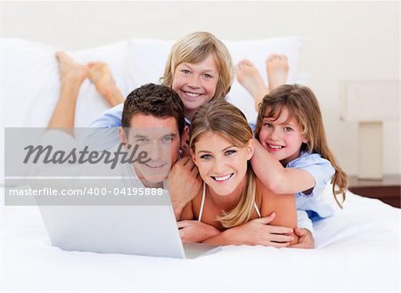 Smiling family looking at a laptop lying down on bed at home