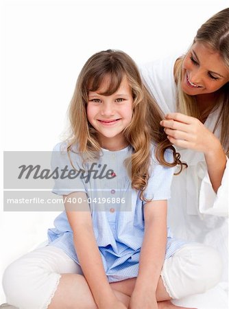 Pretty woman brushing her daugther's hair against a white background