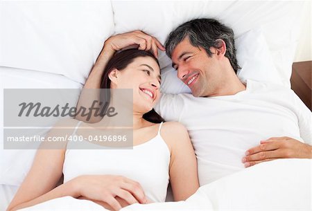 Enamored couple hugging lying in their bed at home