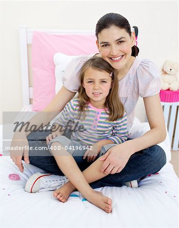 Smiling mother hugging her girl sitting on a bed