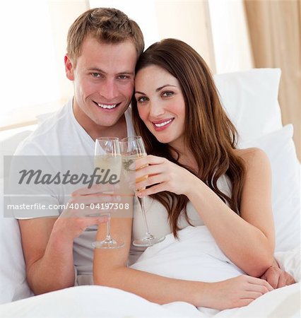 Loving couple drinking champagne lying in bed at home