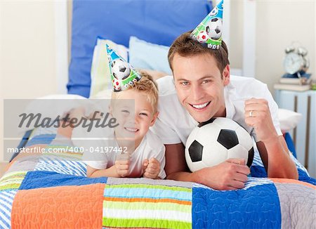 Cute little boy and his father watching a football match in the kid's bedroom