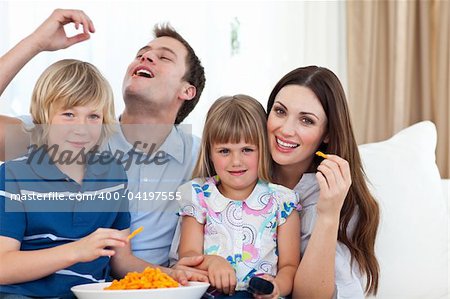 Young family eating crisps while watching TV on the sofa