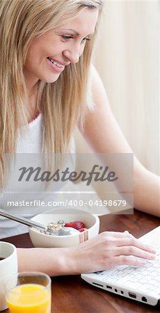 Cheerful woman using a laptop while having a breakfast in a living-room