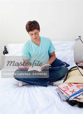 Teenager reading a book from school in his bedroom