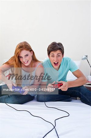 A excited teen couple playing video games in a bedroom