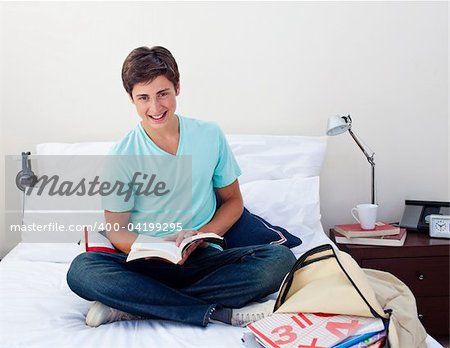 Smiling teenager studying maths in his bedroom sitting on his bed