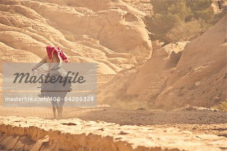 arabian man riding his horse on rocky desert