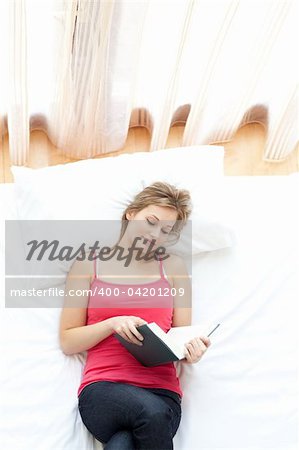 Relaxed woman reading a book lying on her bed