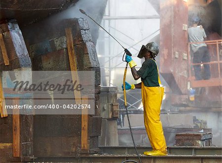shipyard worker powerwashing a ship on drydock