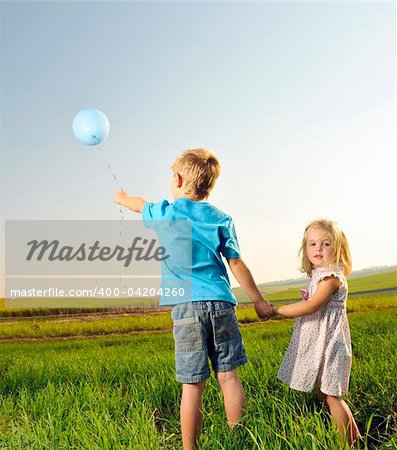 Brother and sister hold hands and hold onto their only balloon