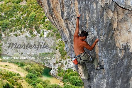 Rock climber moving up the rock, view with mountain river at the background