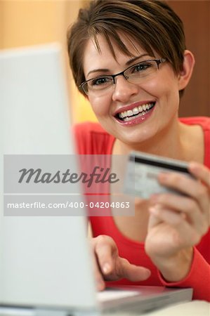 Attractive young woman holds up the credit card she is using to shop with on her laptop computer. Vertical shot.