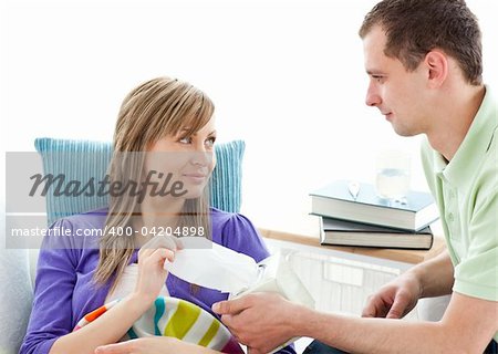Caring man giving his ill girlfriend tissue lying on a sofa against white background