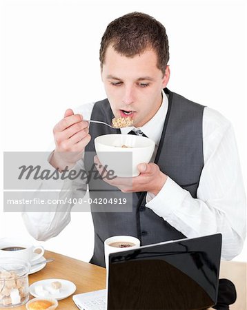 Concentrated businessman eating cereals looking at his laptop against white background