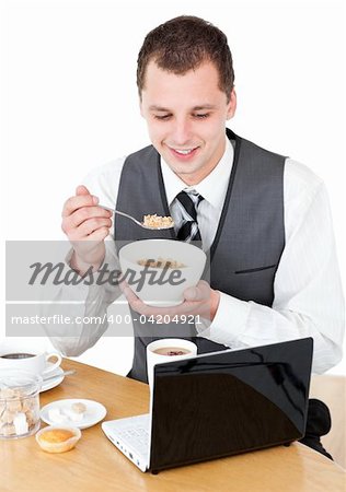 Happy businessman eating cereals looking at his laptop against white background