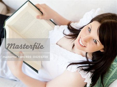 Bright brunette teenager holding a book smiling at the camera in the living room