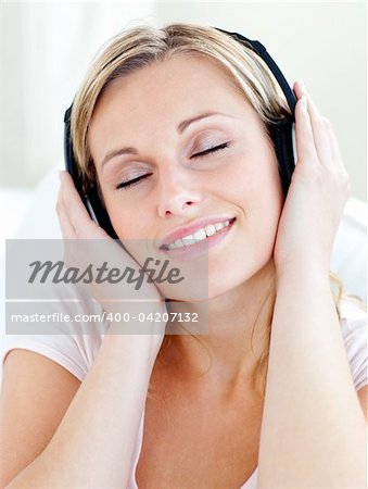Radiant young woman listen to music wearing headphones in the living room
