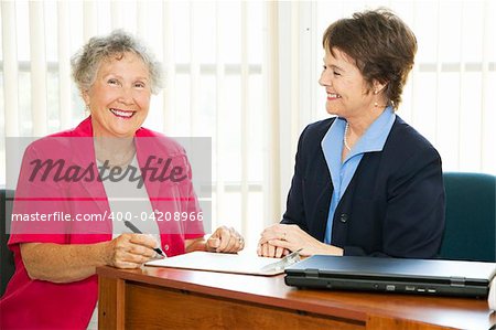 Happy mature businesswomen in the office signing paperwork.