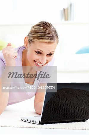 Delighted young woman looking at her laptop lying on the floor in the living-room