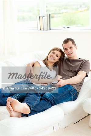 Loving couple lying on the sofa smiling at the camera in the living room