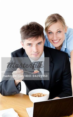 Enamored couple of businesspeople smiling at camera eating cereals against white background