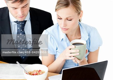 Concentrated couple of businesspeople reading the newspaper drinking coffee against white background