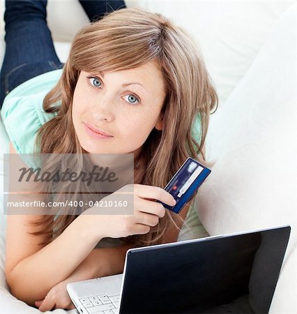 Close-up of a attractive woman lying ona sofa holding a card and laptop in the living room