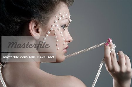 close up portrait of cute brunette with necklace and creative make up looking on one side with pearl on her face