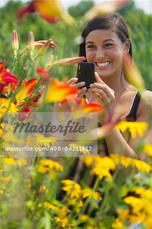 Cute Asian woman smiles while taking pictures of flowers with a small camera. Vertical shot.