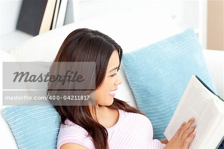 Concentrated asian woman reading a book at home in the living-room