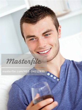 Handsome young man holding a glass of wine sitting on a sofa in the living-room at home