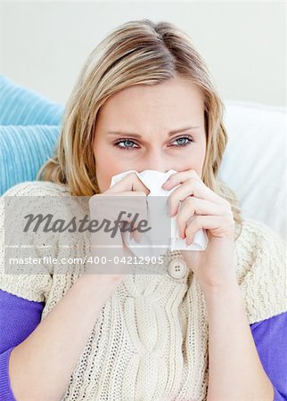 sick woman using a tissue sitting on a sofa at home