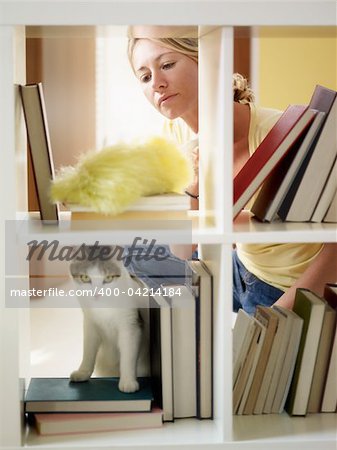 mid adult woman dusting bookshelves. Vertical shape, three quarter length