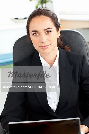 Self-assured hispanic businesswoman sitting at her desk in front of her laptop in her office