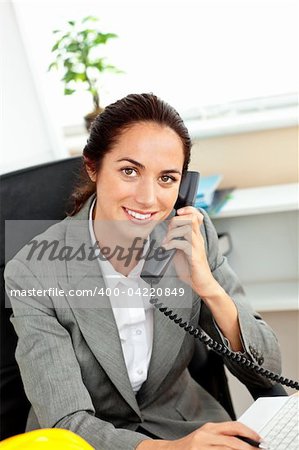 Busy hispanic female architect using her laptop while talking on phone in her office