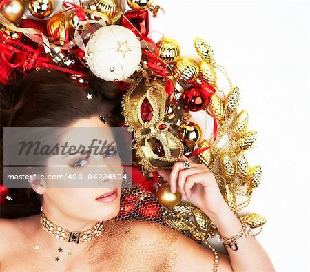 Beautiful brunette lying among Christmas decoration holding mask isolated on white