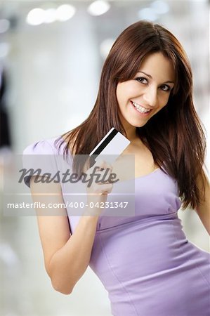 Portrait of the beautiful happy girl in the shop, holding in a hand a credit card