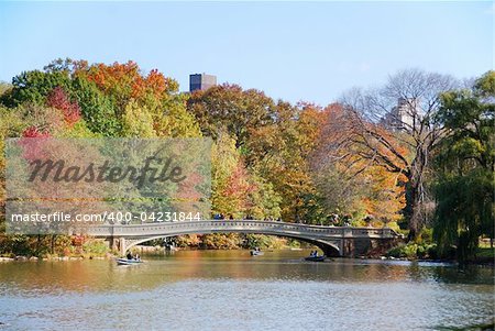 New York City Central Park panorama view in Autumn with Manhattan skyscrapers and colorful trees with Rainbow Bridge over lake with reflection.