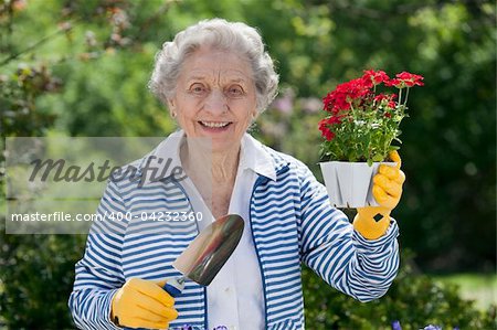 A smiling senior woman is standing with a trowel and holding a starter plant she is getting ready to plant. Horizontal shot.