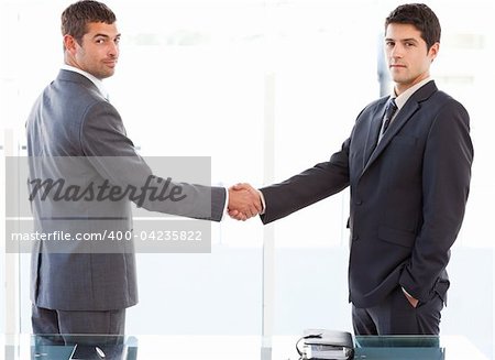 Two charismatic businessmen shaking hands standing in the office at work