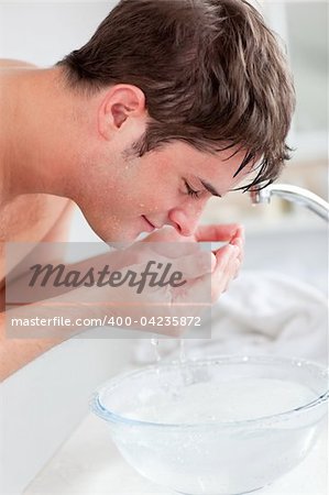 Positive caucasian man spraying water on his face after shaving in the bathroom at home