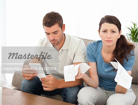 Desperate woman doing her accounts with her boyfriend sitting on the sofa at home