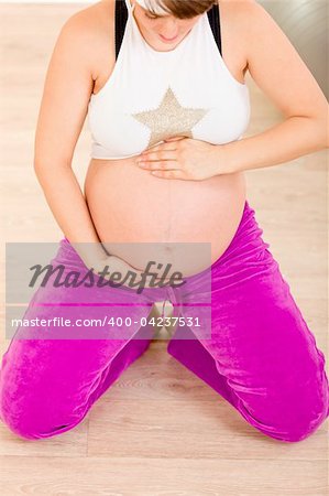 Pregnant woman in sportswear sitting on floor and holding her belly. Close-up.