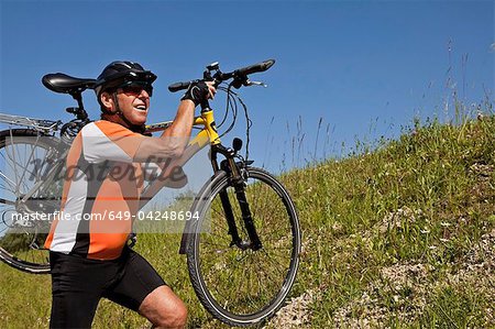 Homme portant le vélo sur la colline herbeuse
