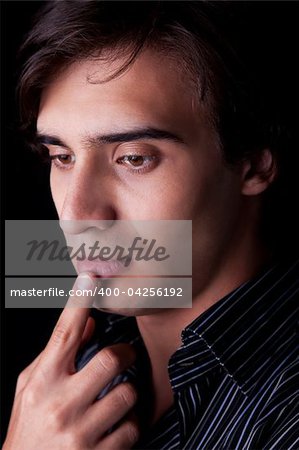 Portrait of a handsome young man thinking, on black background. Studio shot