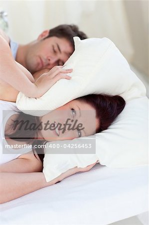 stressed future mom with head under the pillow in bed with her husband snoring during the morning