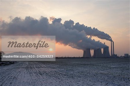 View of coal powerplant against sun with several chimneys and huge fumes