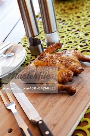 Whole barbeque chicken with cutlery and spices on wooden cutting board